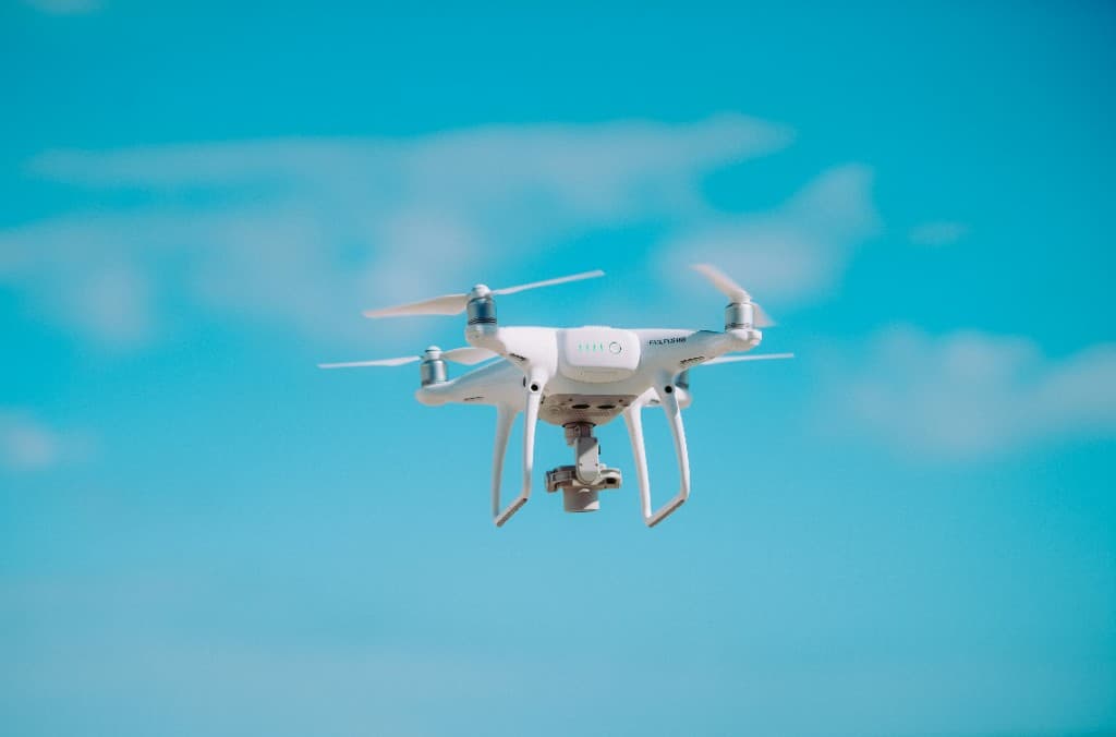 青空を背景にホバリングする白いマルチローター型ドローン